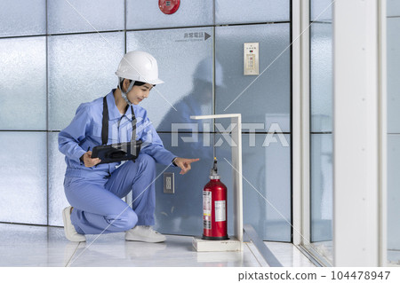 Woman in work clothes inspecting a fire extinguisher Building maintenance image Woman in work clothes inspecting a fire extinguisher Building maintenance image 104478947