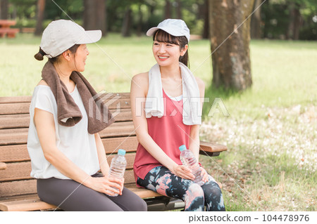 Asian woman sitting on a park bench and resting during exercise, aerobic exercise, running in the park 104478976