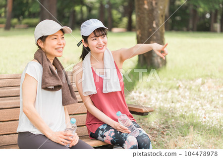 Asian woman sitting on a park bench and resting during exercise, aerobic exercise, running in the park 104478978