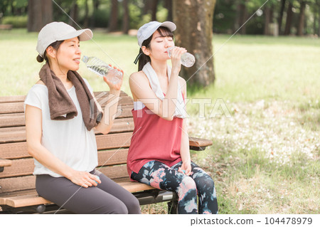 Asian woman sitting on a park bench and resting during exercise, aerobic exercise, running in the park 104478979