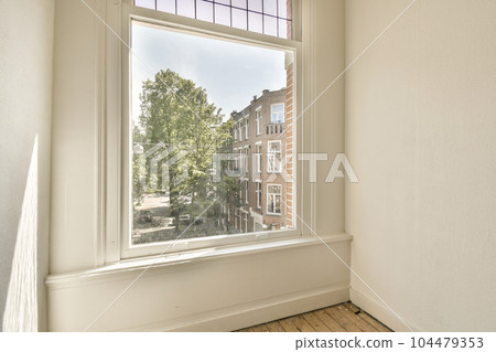 an empty room with a tree in the window and a view of a street outside area through the window pane 104479353