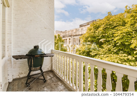 a grill sitting on the porch in front of a white brick building with green trees and blue sky behind it a grill sitting on the porch in front of a white brick building with green trees and blue sky behind it 104479354