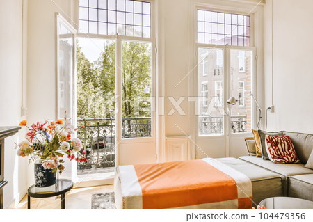 a living room with an orange blanket on the couch and two windows that look out onto the cityscapea a living room with an orange blanket on the couch and two windows that look out onto the cityscapea 104479356