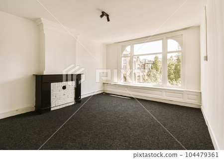an empty room with a fire place in the corner and black carpeting on the floor next to the window 104479361