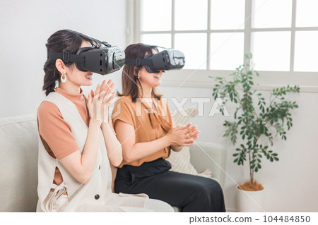 Women wearing VR goggles enjoying simulated trips, VR games, and 3D movies at home 104484850