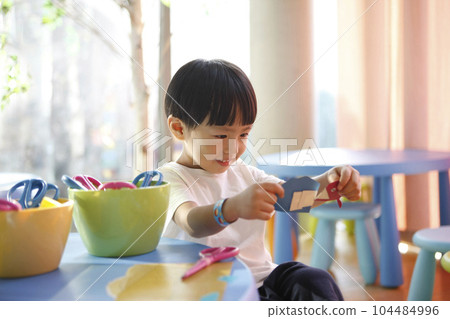 Multicolored art education materials, children's stationery and learning creative drawing and origami play, a cute child in a kindergarten classroom is smiling happily while looking at his creations. 104484996