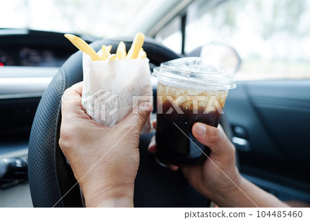 Asian woman driver hold and eat french fries in car, dangerous and risk an accident. 104485460