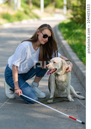 Blind young woman cuddling with guide dog on a walk outdoors.  104485833