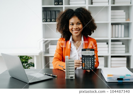 Young real estate agent worker working with laptop and tablet at table in office and small house beside it.. 104487340