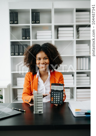 Young real estate agent worker working with laptop and tablet at table in office and small house beside it.. 104487341