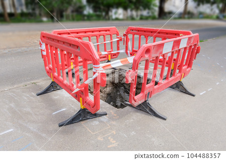 red plastic protective barriers for road works. barriers around pit on the road. red plastic protective barriers for road works. barriers around pit on the road. 104488357