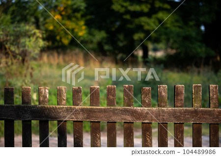 An old wooden village fence and in the background in a blur a green meadow. 104489986