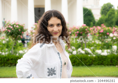 Beautiful successful 35-year-old woman in white shirt walking in the park among roses 104490281