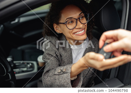 Close up of young smiling woman getting keys of a new car from the salesman. Concept for car rental 104490798