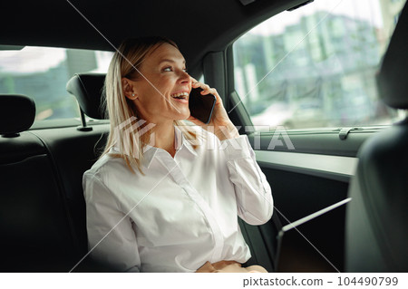 Female entrepreneur working on laptop and talking phone during traveling to office in luxury car 104490799