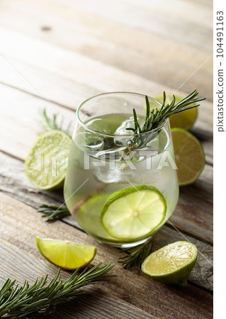 Gin tonic with ice, rosemary, and lime slices on an old wooden table. Gin tonic with ice, rosemary, and lime slices on an old wooden table. 104491163