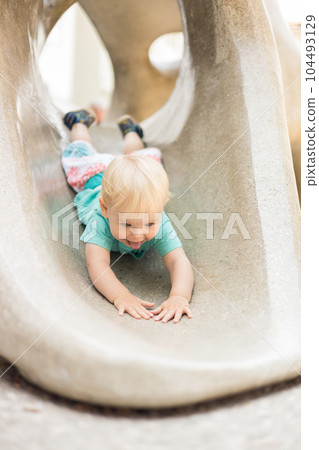 Child playing on outdoor playground. Toddler plays on school or kindergarten yard. Active kid on stone sculpured slide. Healthy summer activity for children. Little boy climbing outdoors 104493129