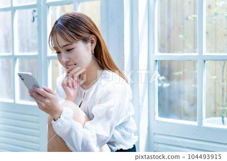 Young woman using a smartphone by the window 104493915