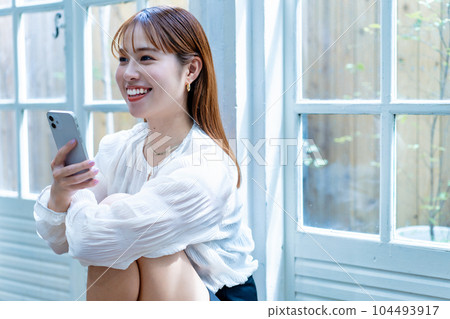 Young woman using a smartphone by the window 104493917