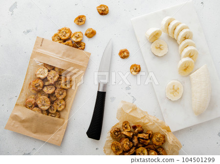 Pack of dried bio banana chip slices with knife and raw banana. Pack of dried bio banana chip slices with knife and raw banana. 104501299