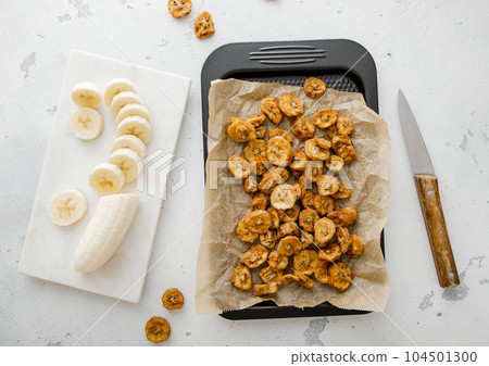 Baking tray with dried banana chip slices and raw peeled banana. 104501300