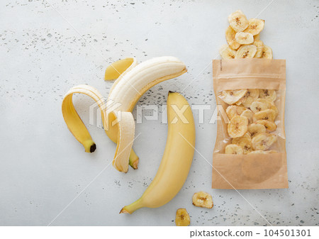 Fresh raw healthy bananas with package of dried banana chips on light board. Fresh raw healthy bananas with package of dried banana chips on light board. 104501301