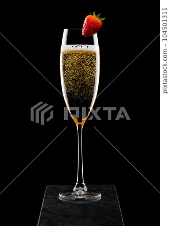Elegant glass of yellow champagne with strawberry on top on black marble board on blac Elegant glass of yellow champagne with strawberry on top on black marble board on blac 104501311