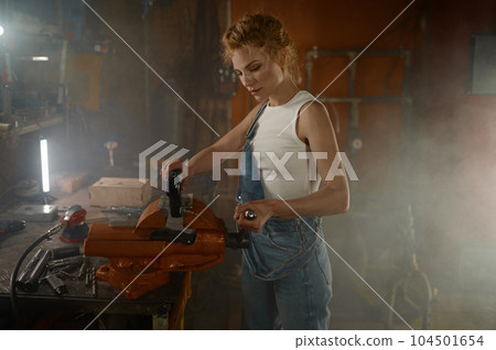 Woman working in garage using vise for clamping spare part 104501654