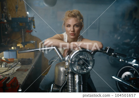 Portrait of beautiful woman biker sitting on motorcycle in garage 104501657