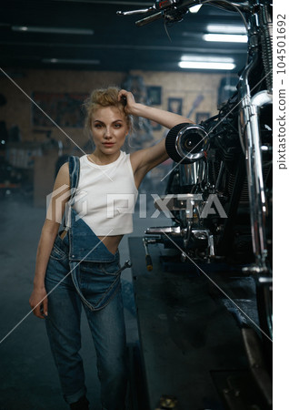 Pretty woman mechanic with wrench in hand at motorcycle workshop 104501692