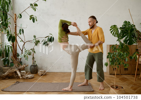 Young woman training yoga with male instructor indoors 104501738