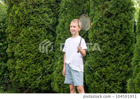 A happy boy holds a badminton racket in his hands, outdoor activities A happy boy holds a badminton racket in his hands, outdoor activities 104501931