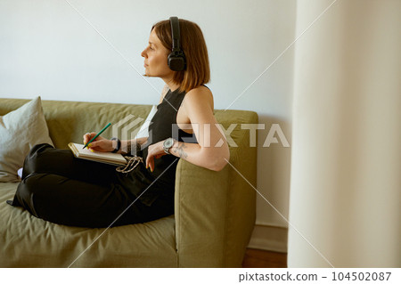 Female student listening webinar in headphones and making notes at home. Distance learning concept Female student listening webinar in headphones and making notes at home. Distance learning concept 104502087