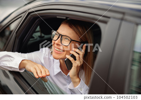 Woman entrepreneur traveling on back seat of car and talking smartphone while looking at window Woman entrepreneur traveling on back seat of car and talking smartphone while looking at window 104502103