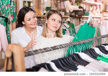 Smiling women choosing green sweater in the modern shop Smiling women choosing green sweater in the modern shop 104502994
