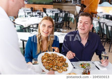 Waiter serving tasty dishes to couple Waiter serving tasty dishes to couple 104503013