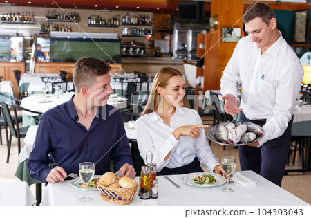 Cheerful waiter serving fish dishes Cheerful waiter serving fish dishes 104503043