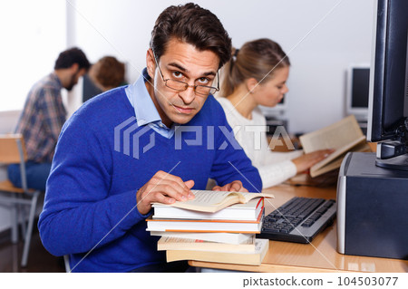 Serious adult student reading textbooks while studying in university computer class Serious adult student reading textbooks while studying in university computer class 104503077