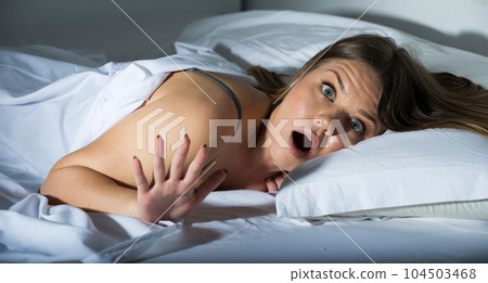 Young female is worried on bed, because oversleep in bedroom 104503468