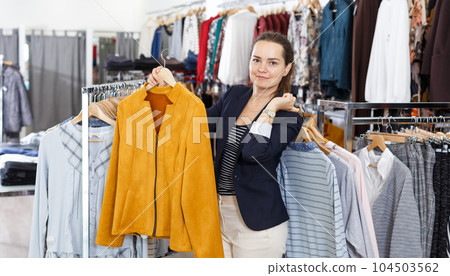 Woman demonstrating clothes on hangers in boutique Woman demonstrating clothes on hangers in boutique 104503562