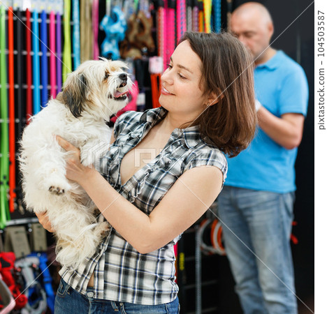 Happy young woman with dog in pet store during shopping with man 104503587