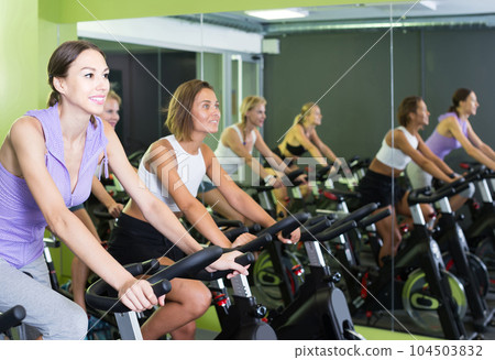 women on cardio training on exercycles in health club 104503832