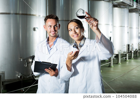 Winery workers taking notes while discussing wine sample 104504088