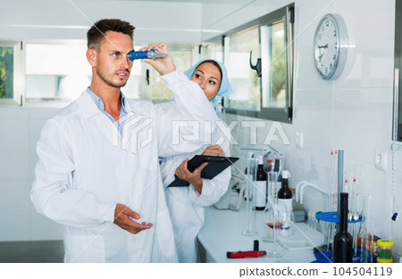 Two researchers in white coat checking wine acidity in laboratory Two researchers in white coat checking wine acidity in laboratory 104504119