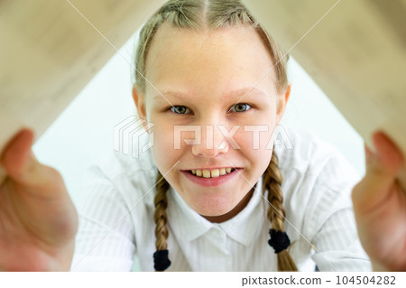Portrait of a cheerful girl with a book in her hands. A happy beautiful girl smiles and looks at the camera through a book Portrait of a cheerful girl with a book in her hands. A happy beautiful girl smiles and looks at the camera through a book 104504282