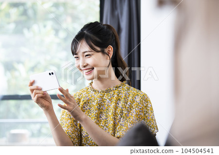 看著她的智能手機帶著微笑的年輕女子 看著她的智能手機帶著微笑的年輕女子 104504541