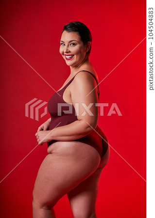 Half-turned smiling lady in underwear standing over red studio background Half-turned smiling lady in underwear standing over red studio background 104504883