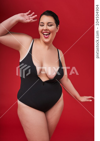 Overjoyed millennial plus-size woman wearing lingerie dancing with closed eyes 104504904