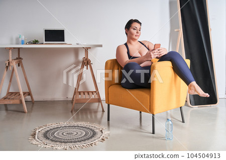 Full length view of the body positive woman sitting at the armchair Full length view of the body positive woman sitting at the armchair 104504913