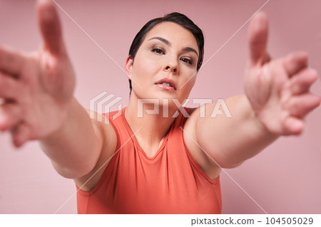 Young overweight woman stretching arms to camera against pink studio background 104505029